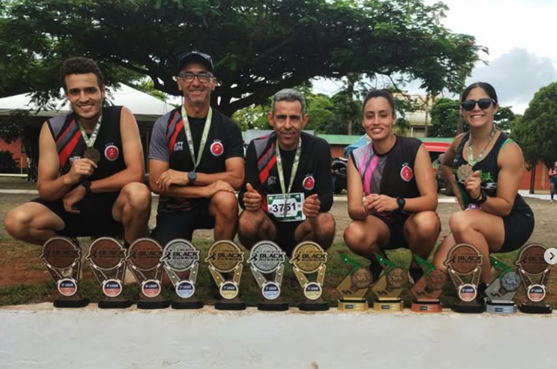 Cinco atletas da ACCB agachados atrás de uma fileira de troféus