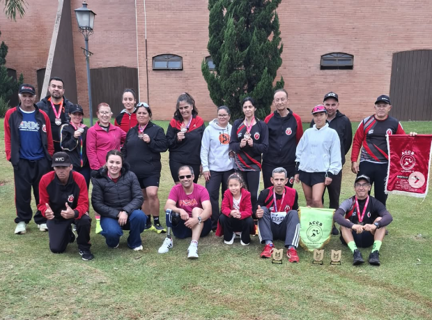Atletas da ACCB reunidos com bandeiras e troféus em um gramado